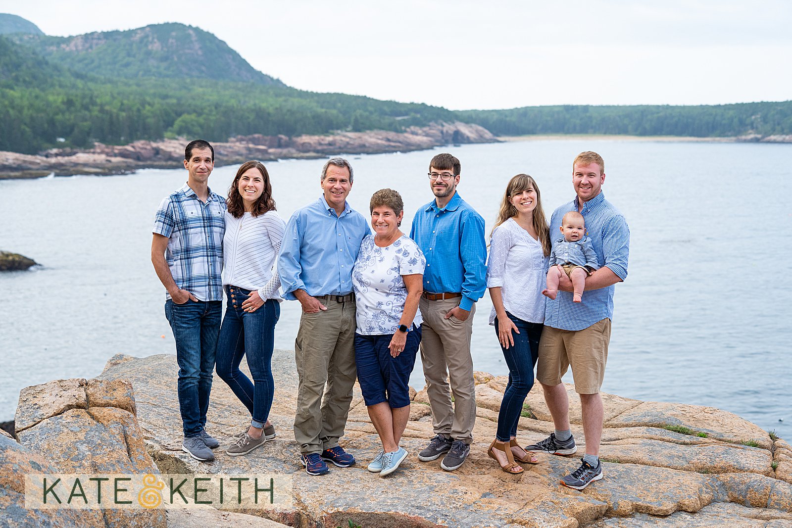 adult family posing on rocks with Acadia National Park as a backdrop