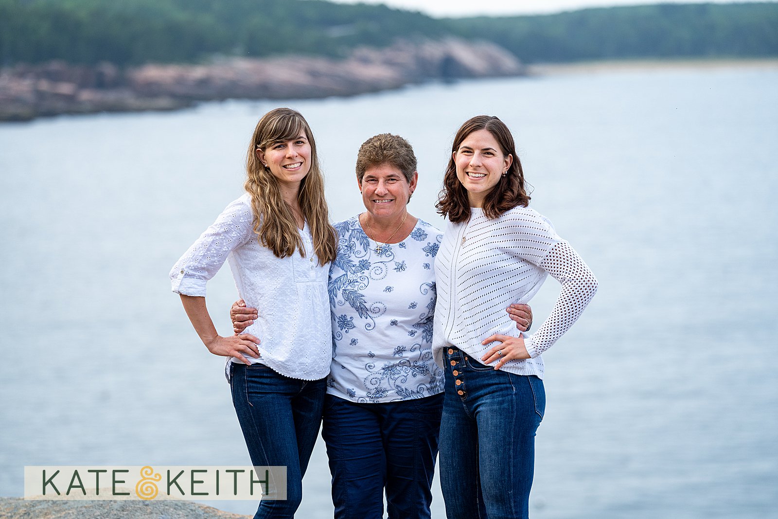 adult twin sisters and their mom posing on rocks with Acadia National Park as a backdrop