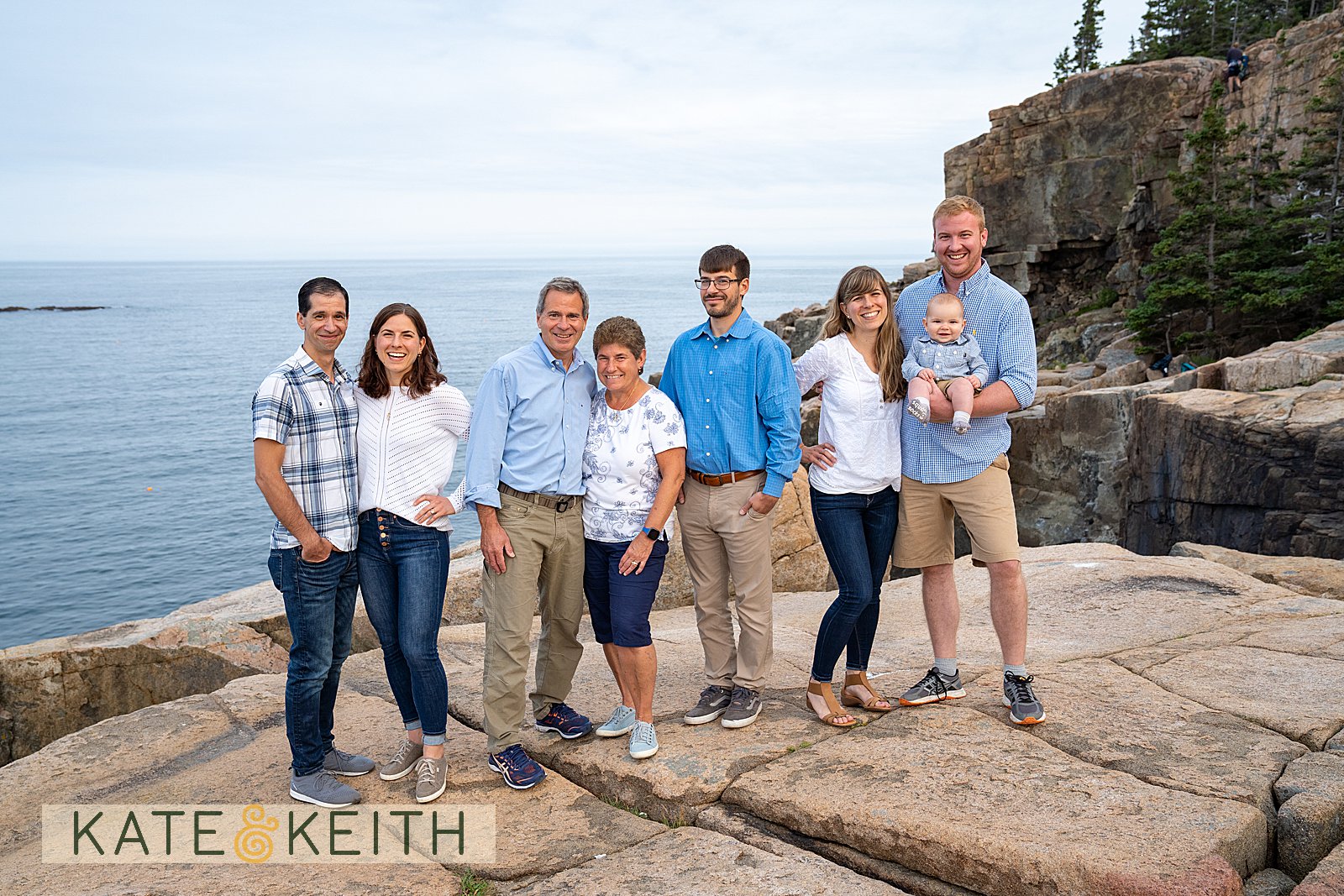 adult family posing on rocks with Acadia National Park as a backdrop