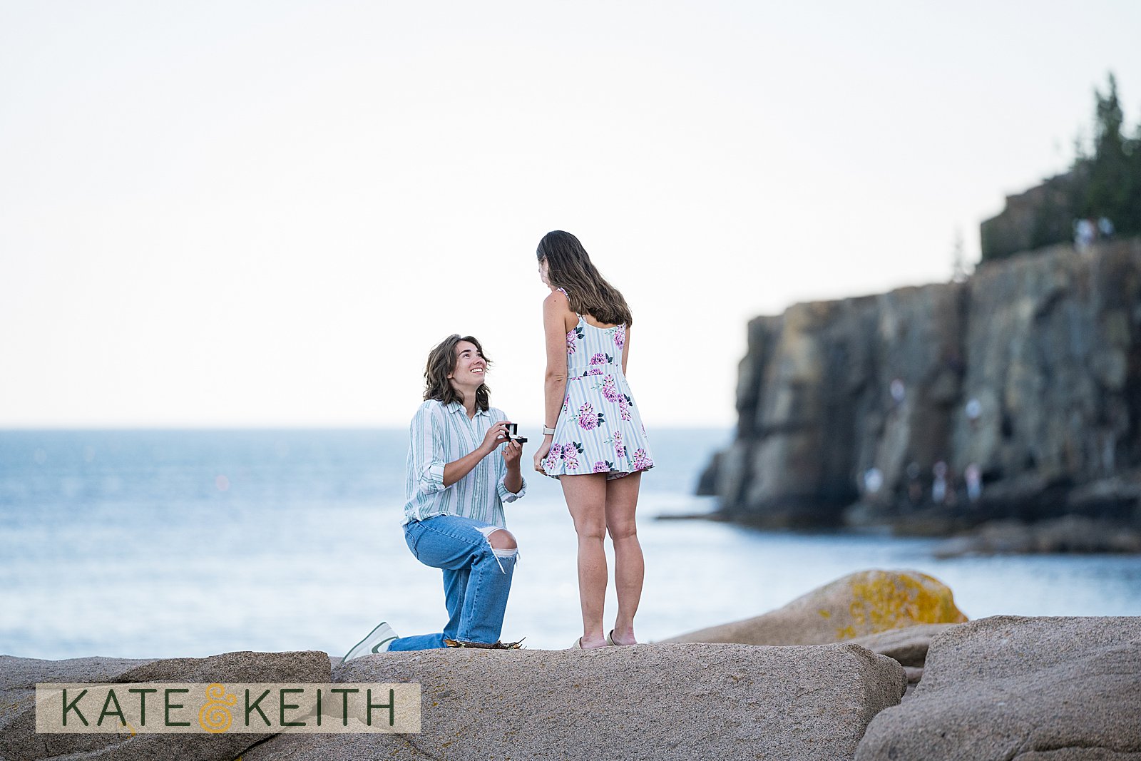 woman on one knee proposing to her girlfriend in Acadia National Park, with cliff and ocean in the background
