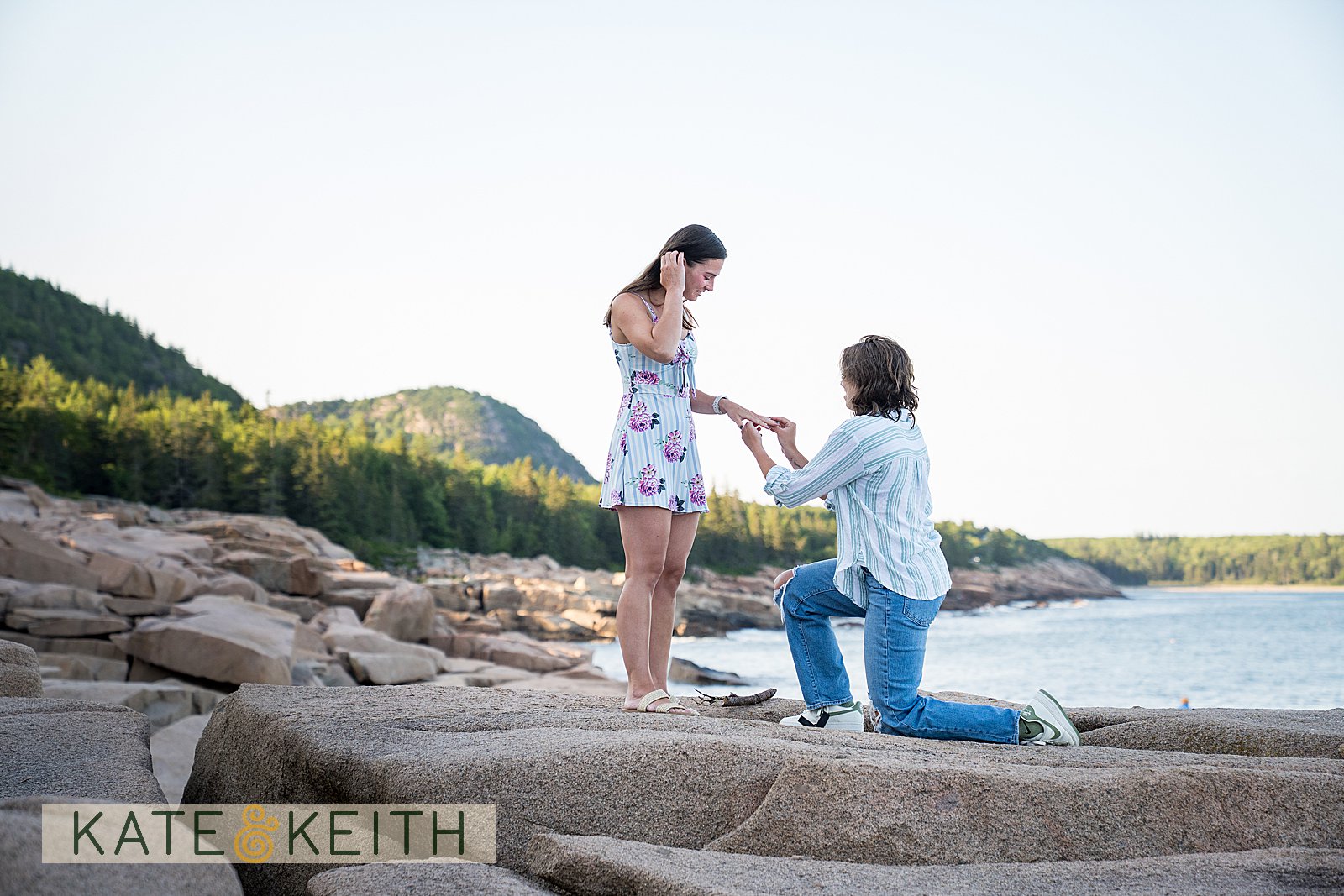 woman on one knee proposing to her girlfriend in Acadia National Park, with mountains and ocean in the background