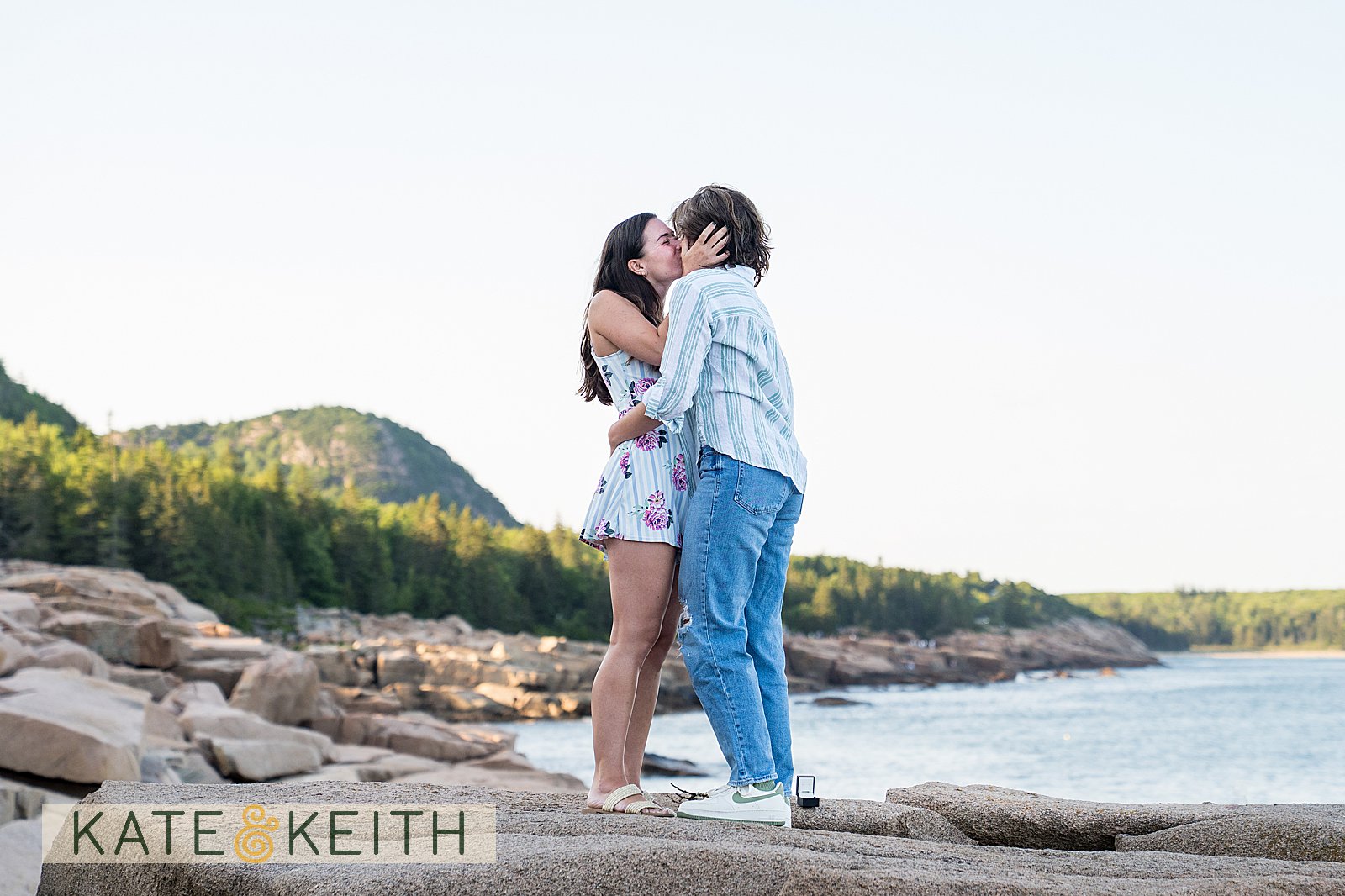 two women kissing after their proposal in Acadia National Park, with the Maine coast behind them