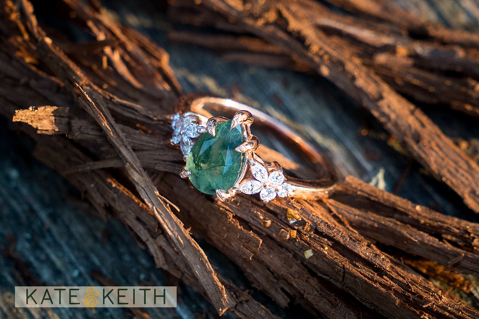 close up of an engagement ring on a log, with a oval green gem flanked by flowery diamonds