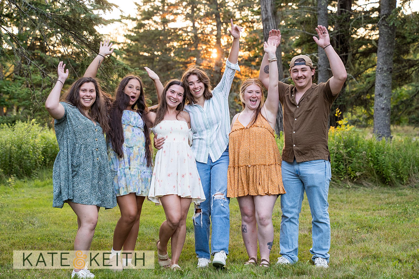 a group of friends standing in the woods of Acadia National Park celebrating with arms in the air
