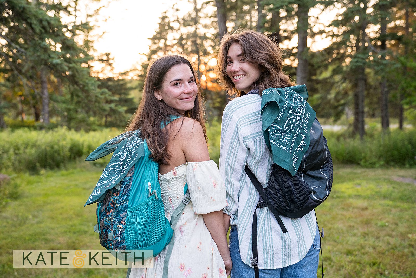 two women walking away wearing backpacks with bandanas announcing their engagement